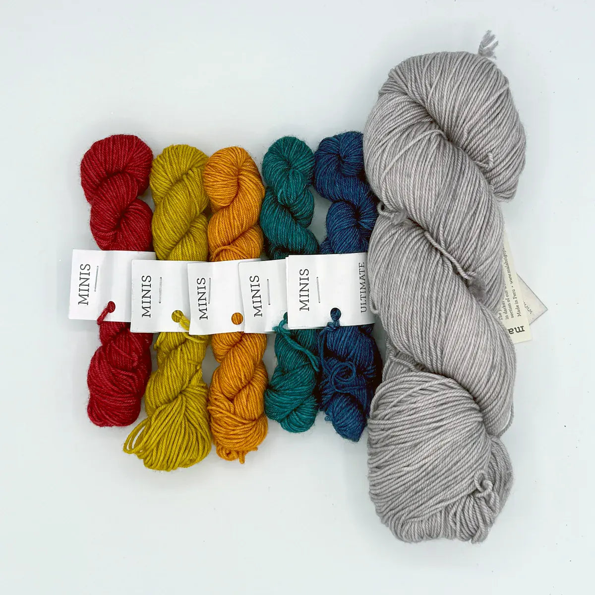 Set of colorful yarn mini skeins and a larger gray skein on a white background