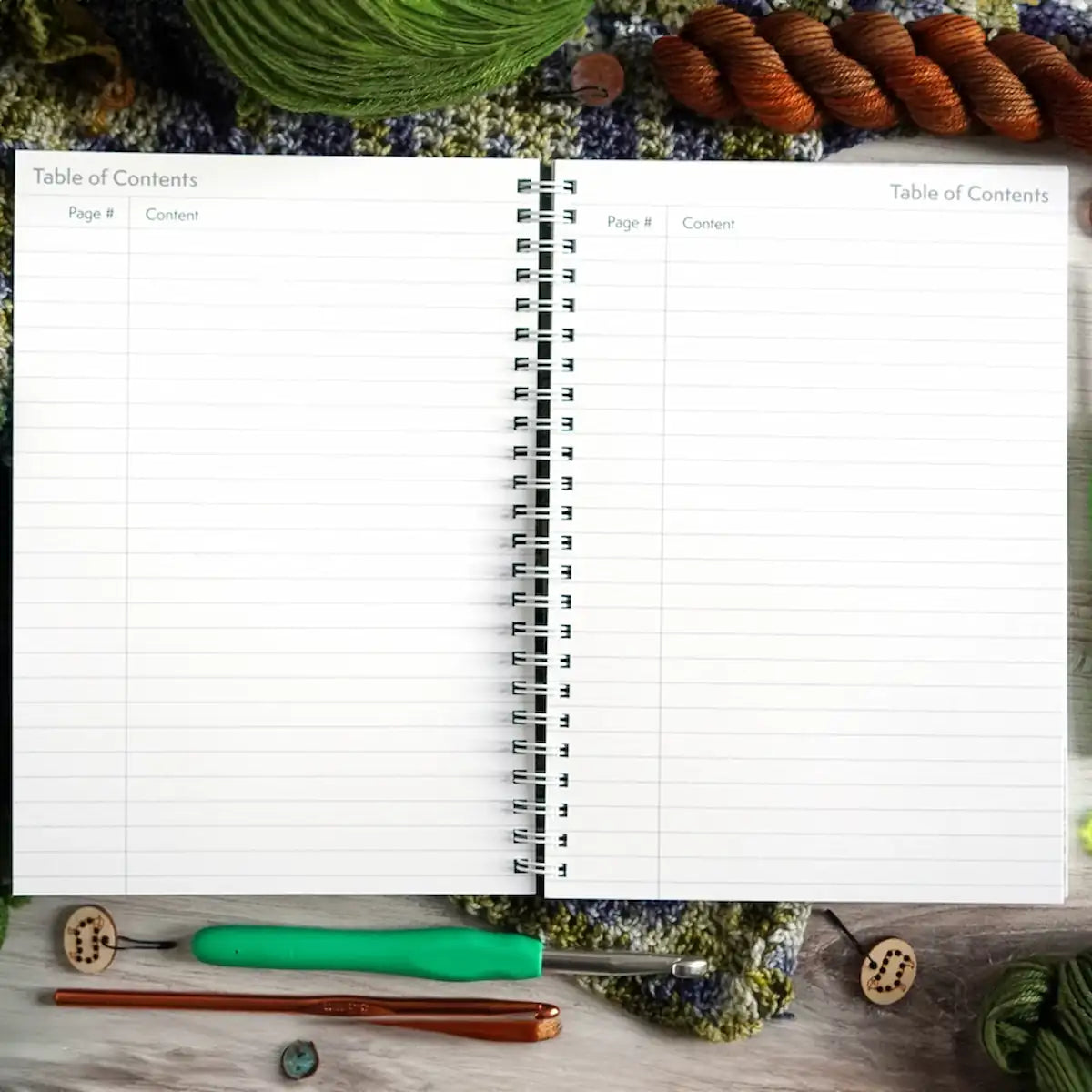 Open notebook with a table of contents on a textured surface with yarn and knitting tools.