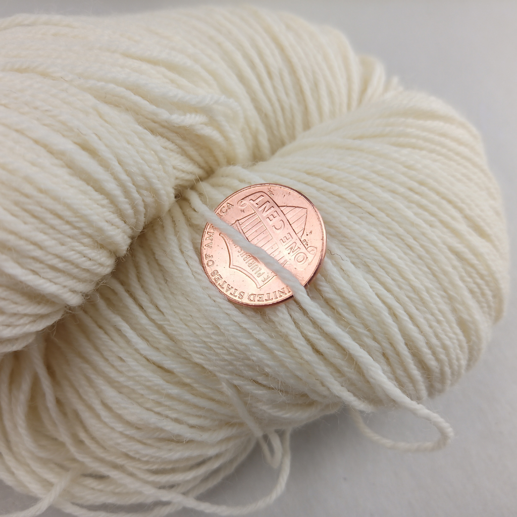 Cream colored yarn with a penny for scale