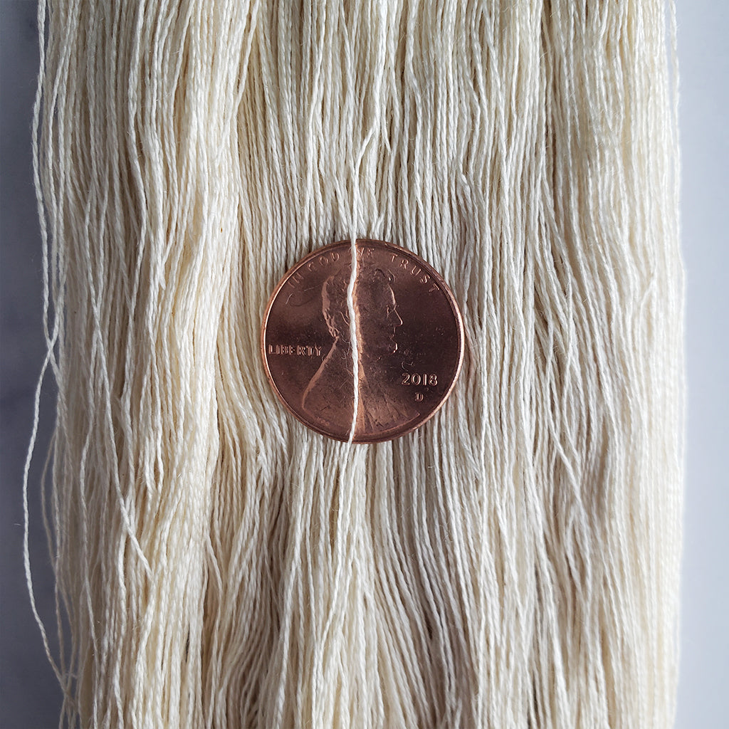 A closeup of Paradise Fibers Superfine Silk Yarn 60/2 with a penny for size.
