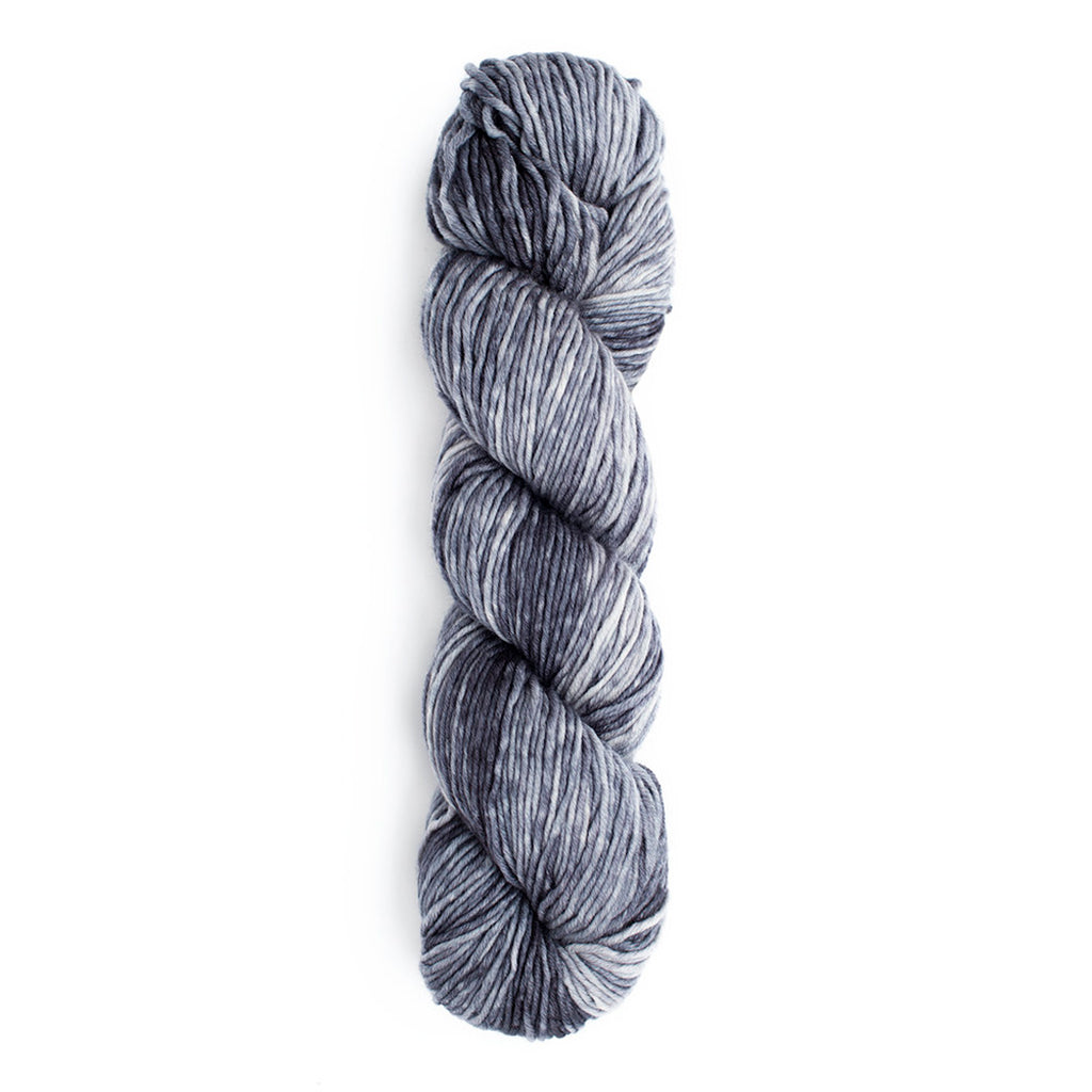 A skein of Monokrom Worsted, color 4064, a tonal cool-toned grey yarn with medium to light greys.