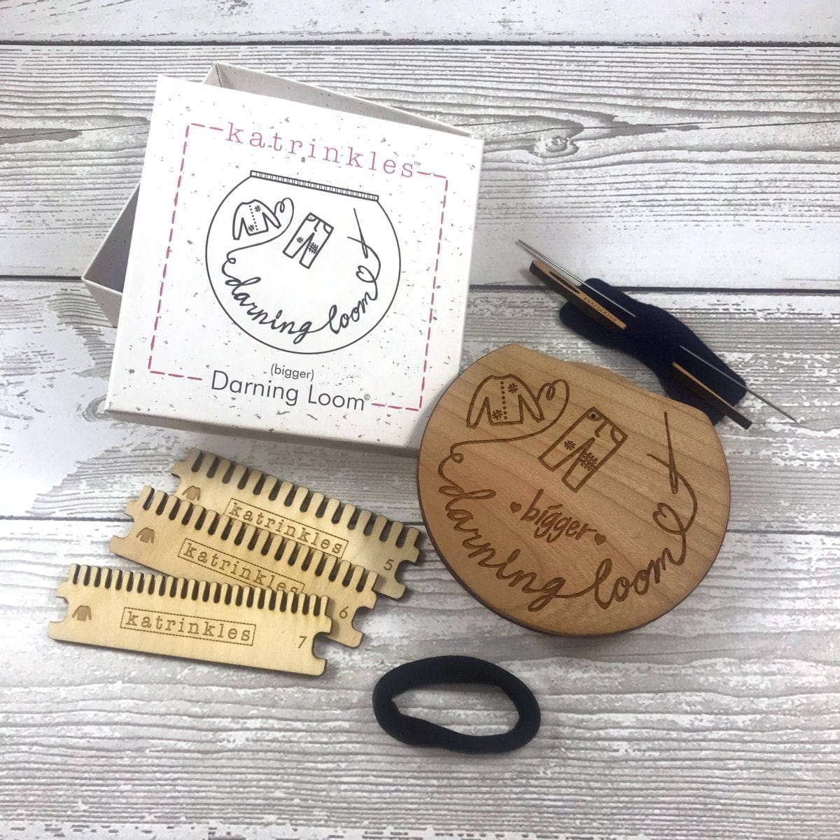 A bigger darning and mending loom kit with all items spread on a wooden surface.