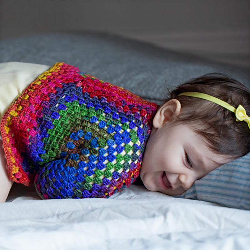 A hand crocheted Squared Up Baby Jacket on a laughing baby.