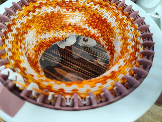closeup of someone using colorful orange yarn to follow knitting loom patterns