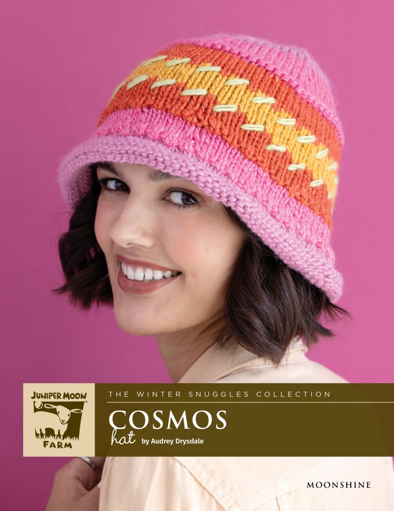 Woman smiling, wearing a pink, orange, and yellow knit hat.