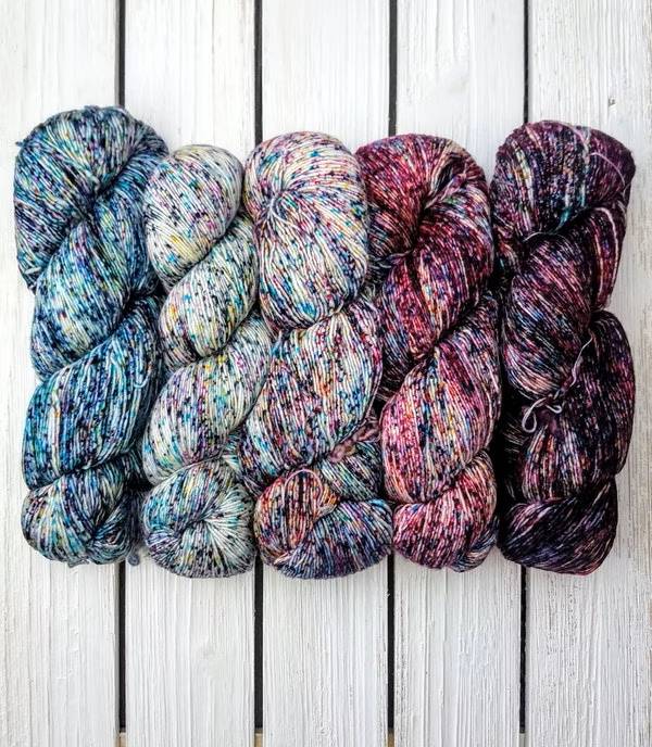 Five skeins of variegated yarn on white wood.