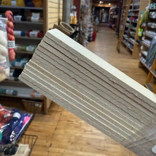 Stack of white cardboard sheets held in front of a store interior with shelves and products.