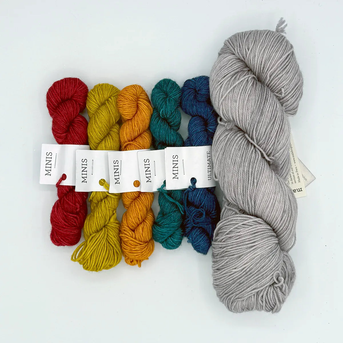 Set of colorful yarn mini skeins and a larger gray skein on a white background