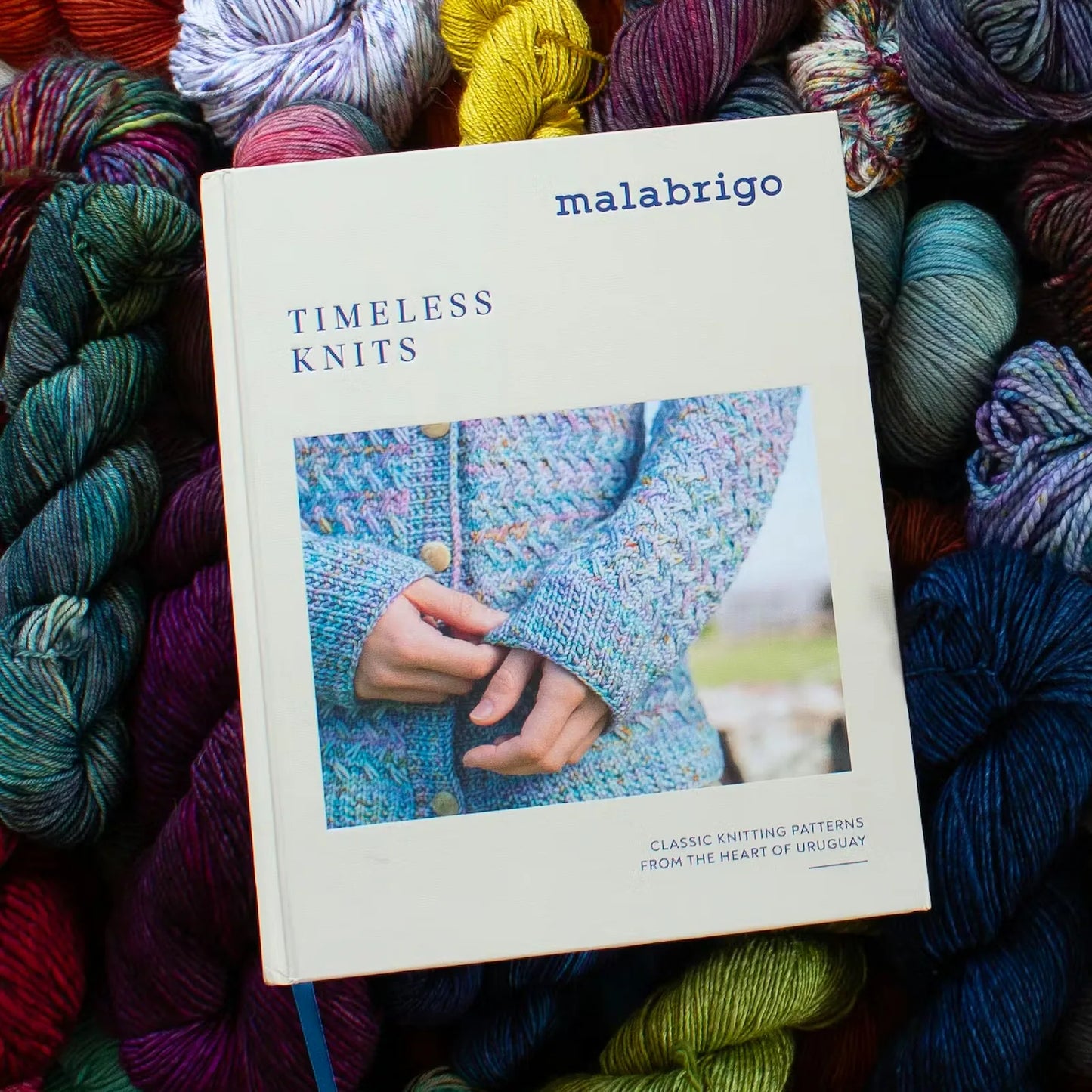Book titled 'Timeless Knits' by Malabrigo surrounded by colorful yarn balls.