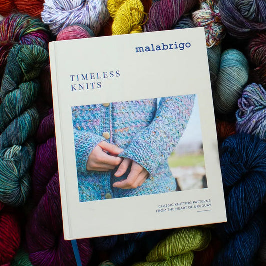 Book titled 'Timeless Knits' by Malabrigo surrounded by colorful yarn balls.