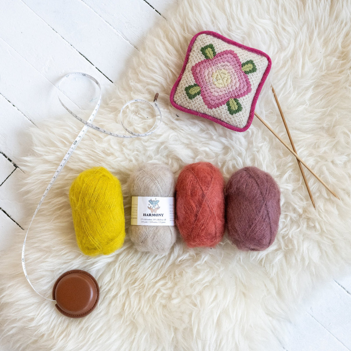 Kelbourne Woolens Harmony Lace Yarn, four balls of kid mohair and silk lace yarn on a sheepskin with knitting needles and a tape measure