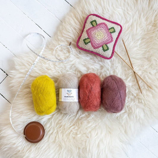 Kelbourne Woolens Harmony Lace Yarn, four balls of kid mohair and silk lace yarn on a sheepskin with knitting needles and a tape measure