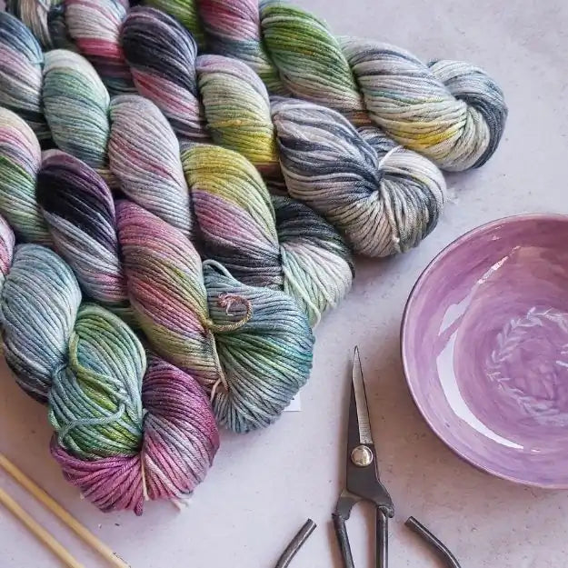 Colorful skeins of yarn with a bowl and scissors on a light surface