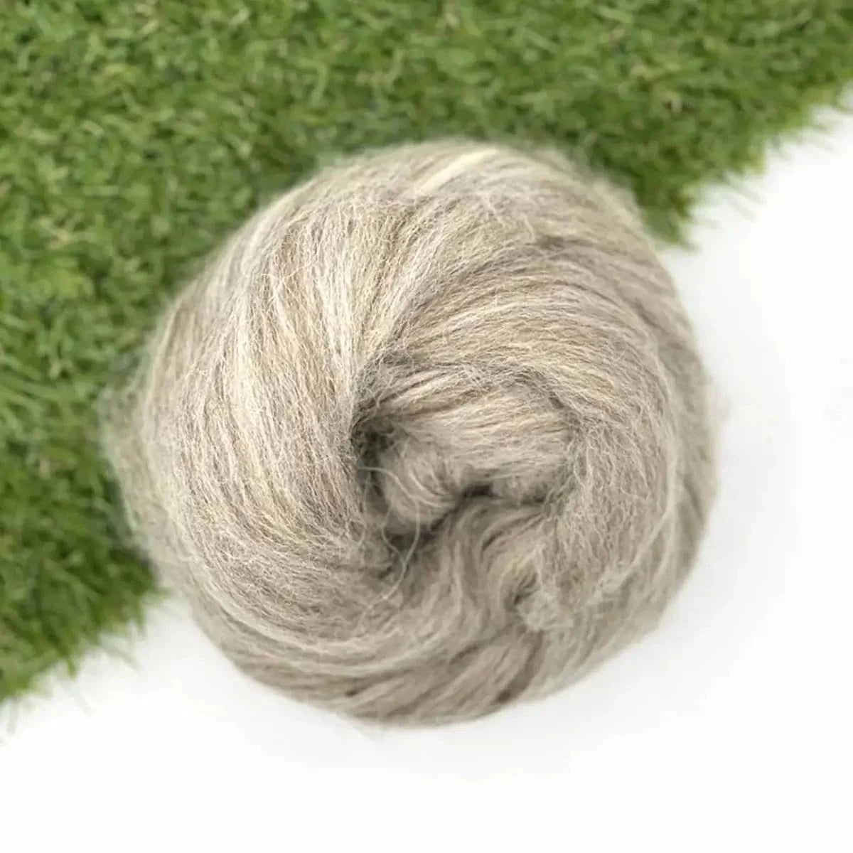 Ball of gray wool on a white background with green grass in the corner