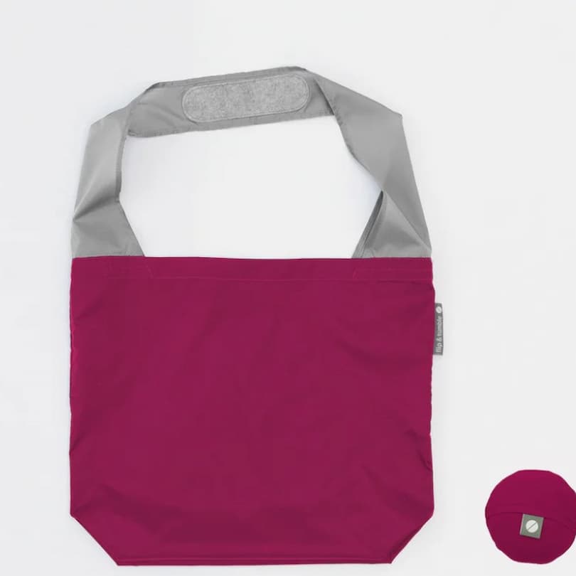 Flip & Tumble tote style bag laid flat. Bag is berry colored with light grey shoulder strap.