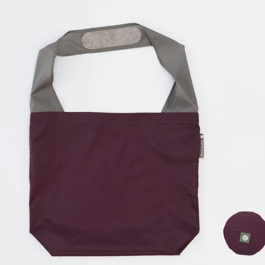 Flip & Tumble tote style bag laid flat. Bag is eggplant colored with light grey shoulder strap.
