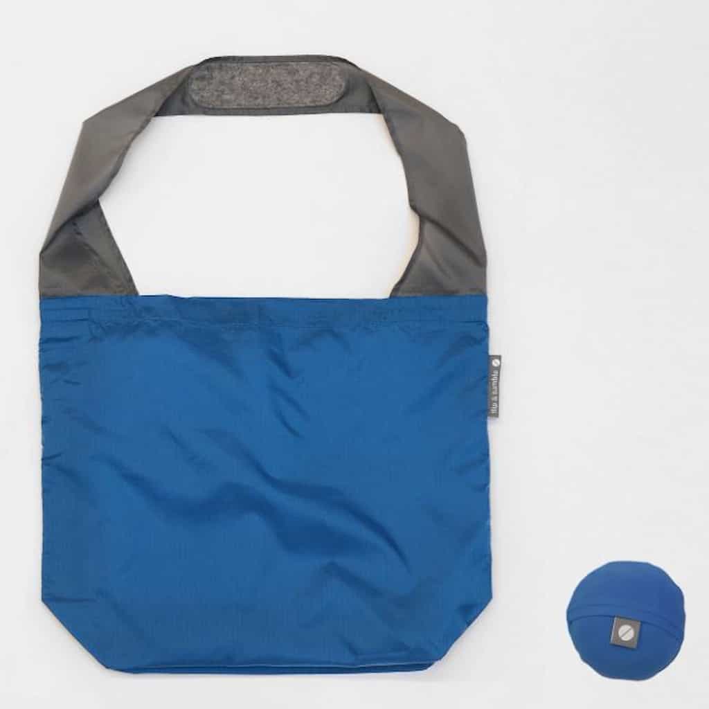 Flip & Tumble tote style bad laid flat. Bag is navy blue colored with a grey shoulder strap. 