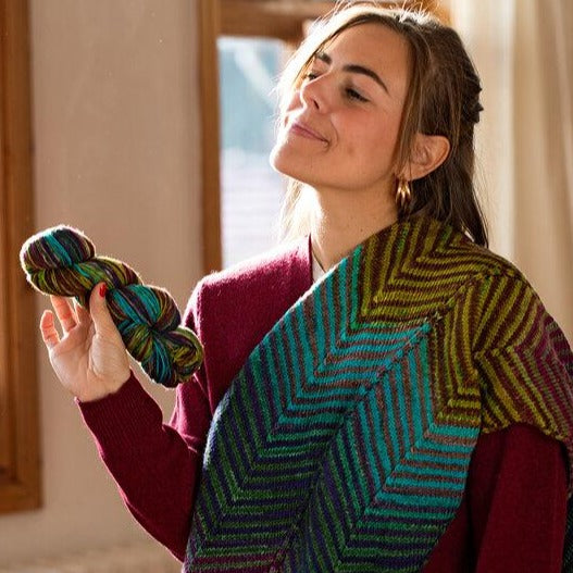 Chevron Scarf knit up from kit #3012 on a smiling model holding a skein of Uneek yarn.