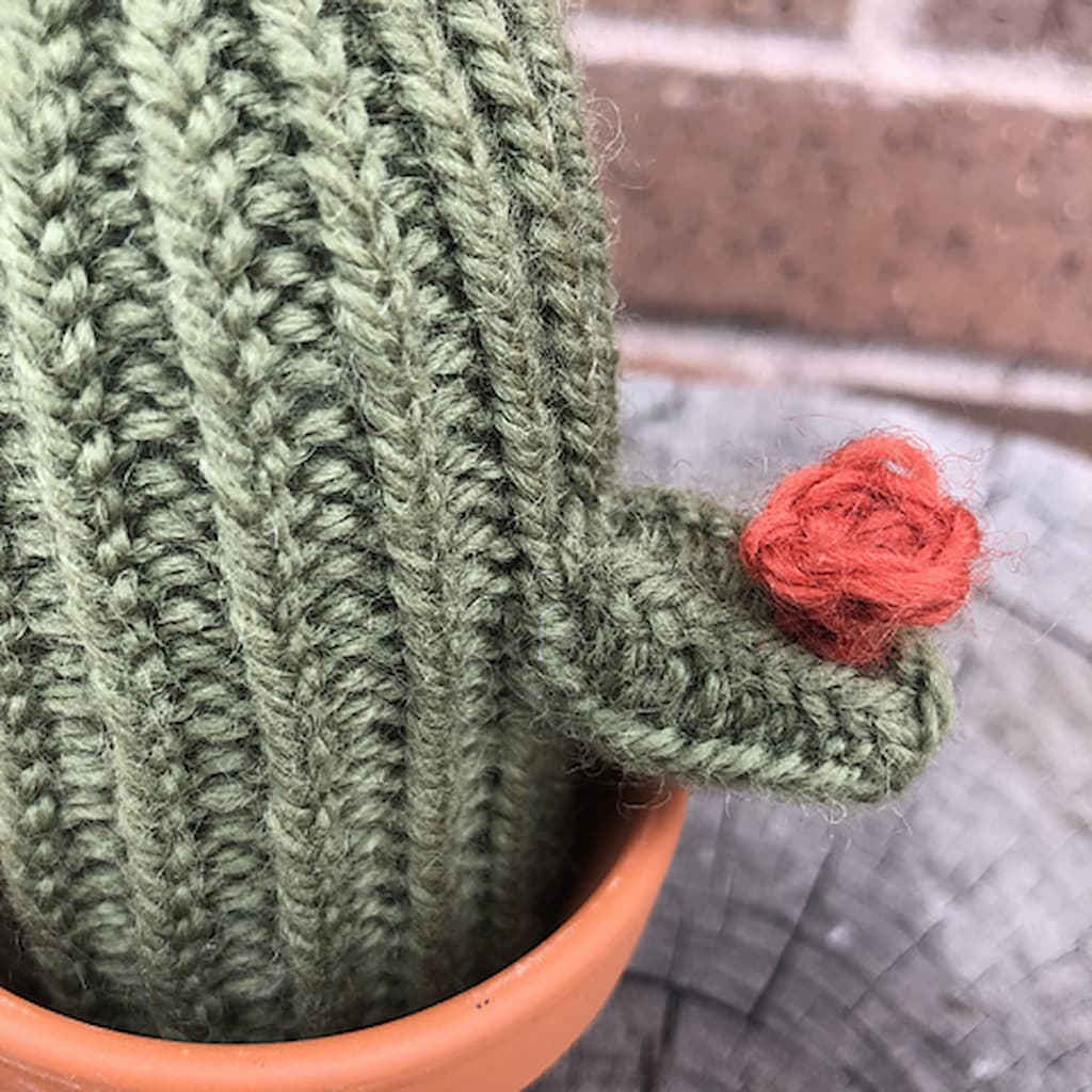 Close up of small pink crocheted flower attached to a small knitted cactus in a small terracotta pot