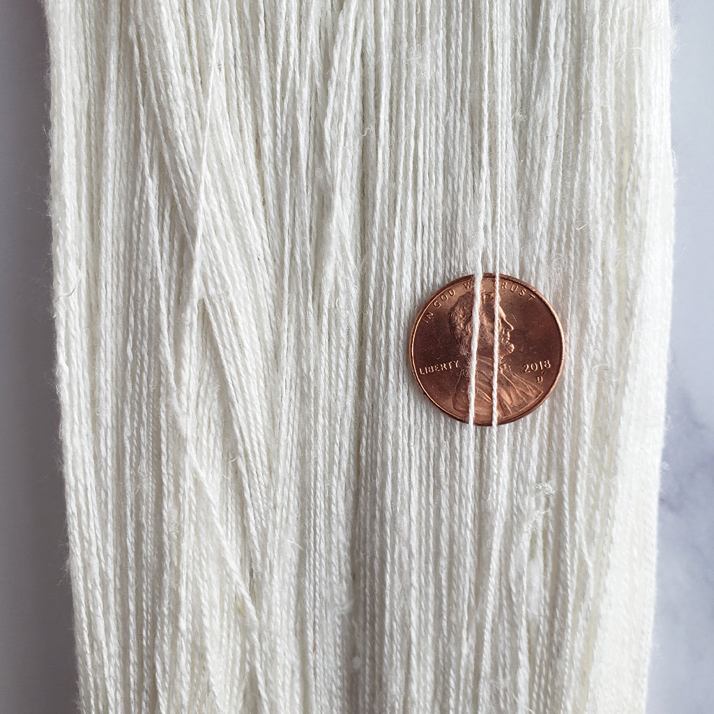 A close up of Paradise Fibers 28/2 Undyed Silk Throwster Yarn with a penny for size.