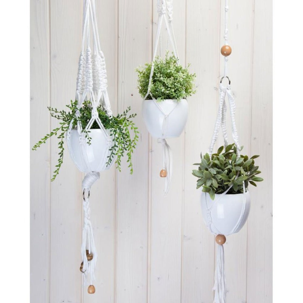 Three white Macrame Hanging Basket holders hanging by a wooden wall.