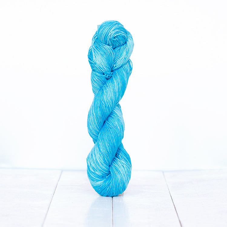 1209, a bright cyan blue skein of Urth Yarn's hand-dyed Monokrom Cotton DK weight yarn.