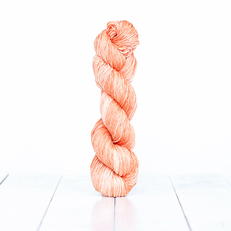 1213, a warm peachy orange skein of Urth Yarn's hand-dyed Monokrom Cotton DK weight yarn.