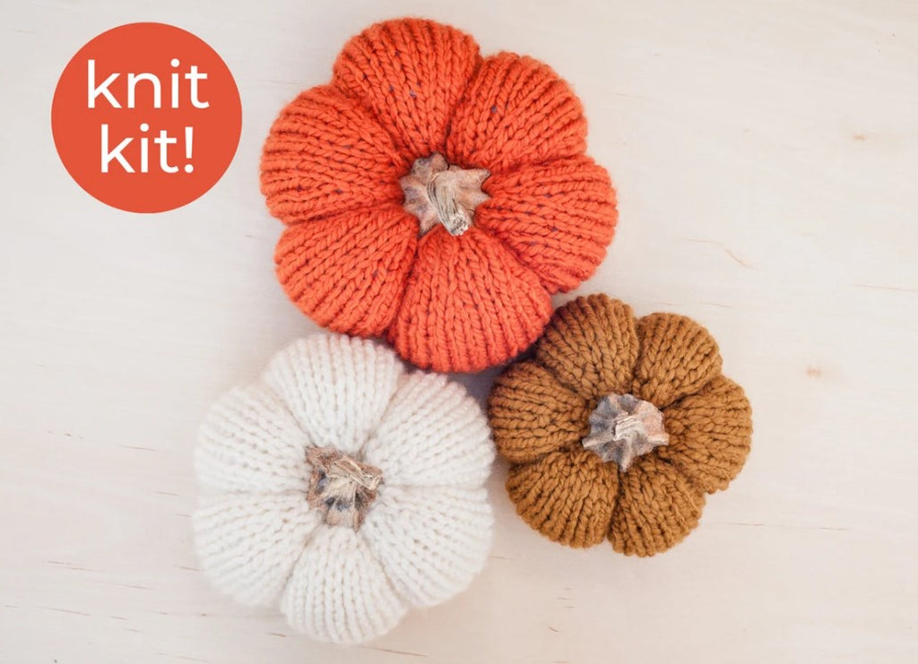 Top view of three knitted pumpkins.  Large on in orange, medium one is white and small one is flax