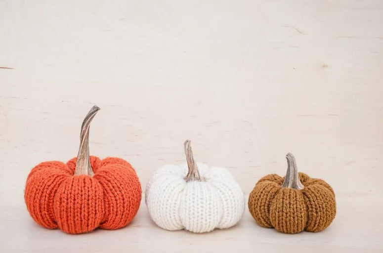 Side view of three knitted pumpkins. Left to right: Orange-large, white-medium, flax small