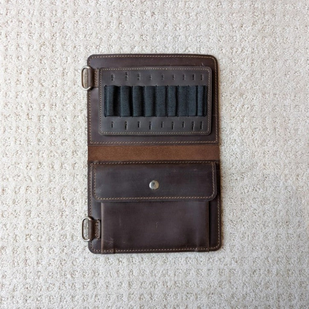 A dark brown leather needle case open to show black elastic needle holders and a large pocket