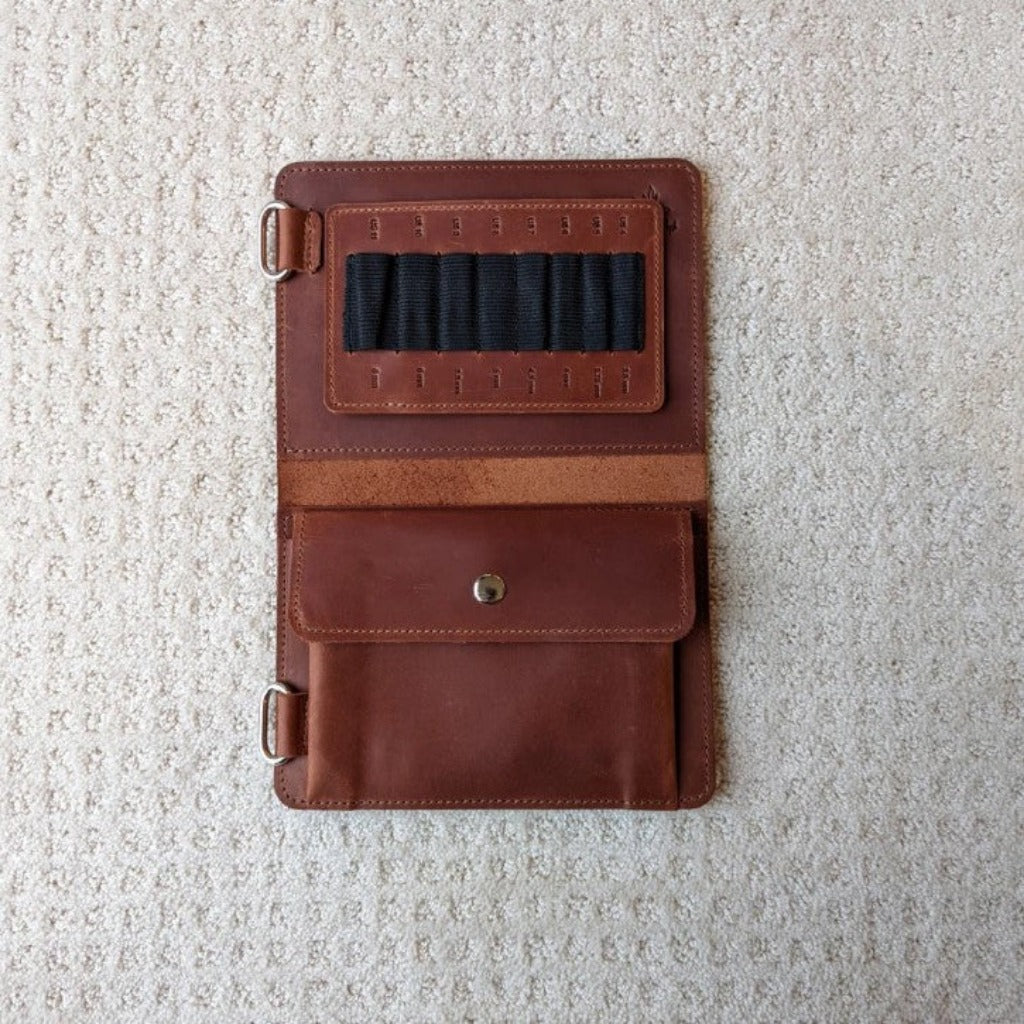 A whiskey brown leather needle case open to show black elastic needle holders and a large pocket