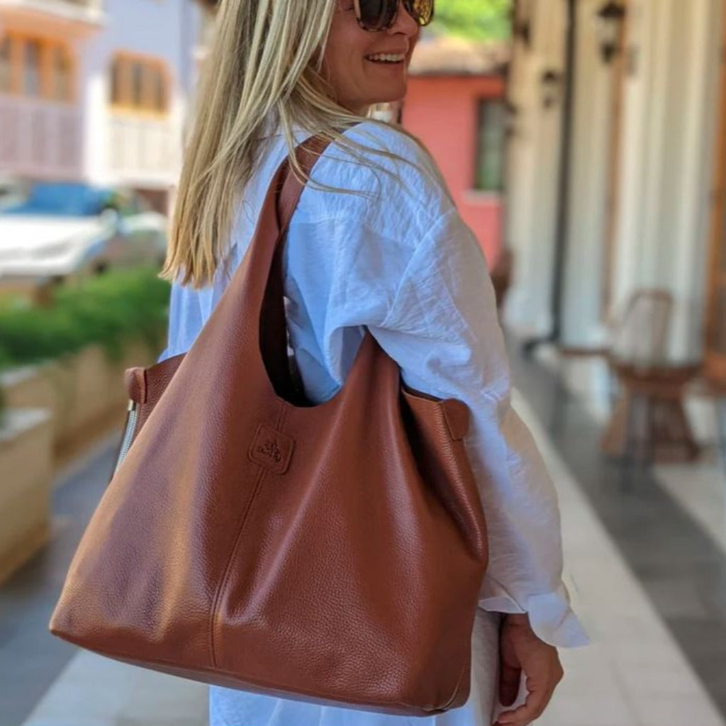 Blonde Woman holding a tan colored Boundless leather bag over her shoulder in the color Almond.