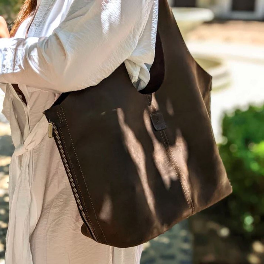 Woman holding a brown colored Boundless leather bag over her shoulder in the color Chocolate.