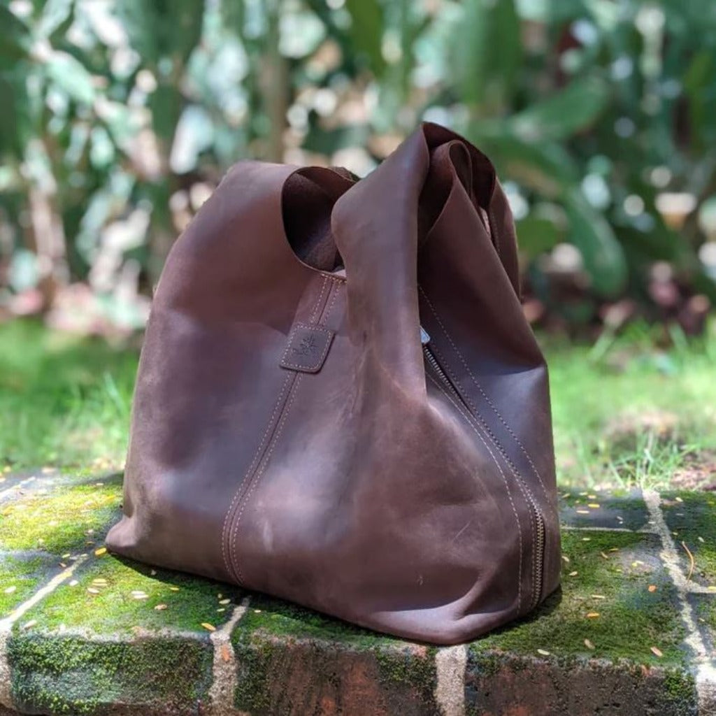 The Boundless leather bag in the color Chocolate sits loosely on a mossy stone ledge.
