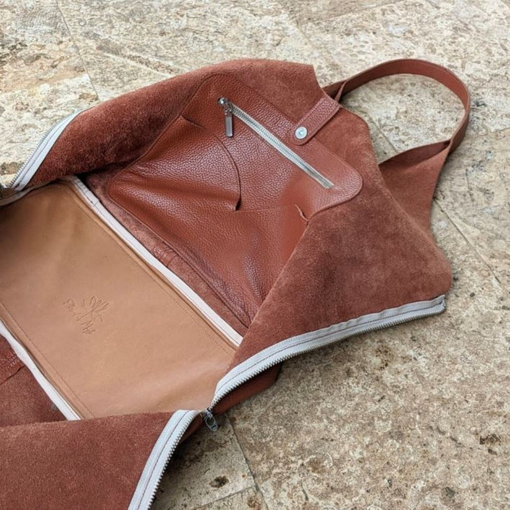 The Boundless leather bag in the color Almond unzipped to lay flat to show the inside pockets