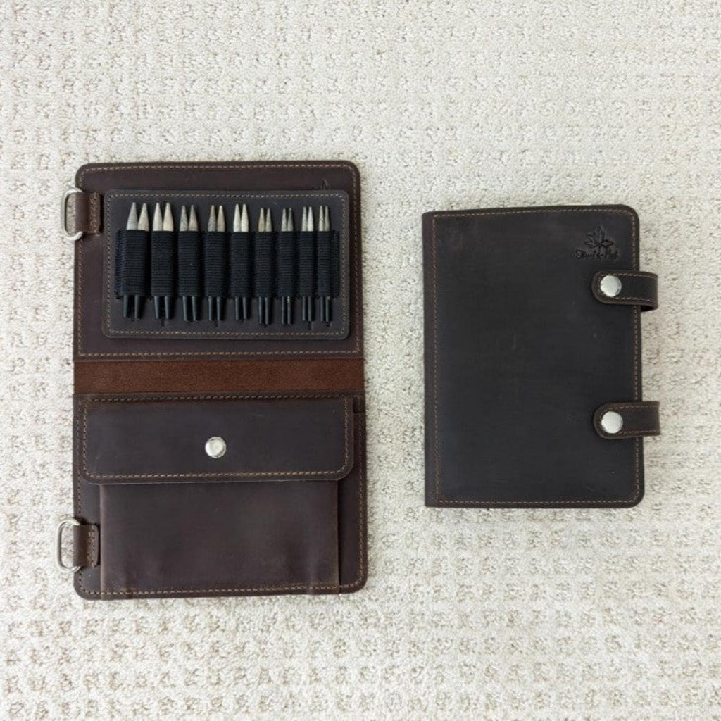 A chocolate leather needle case open to show black elastic slots to hold needles 