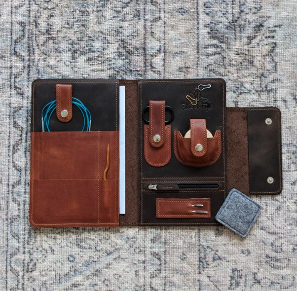 A chocolate brown and whiskey colored leather notions case open faced to reveal the contents