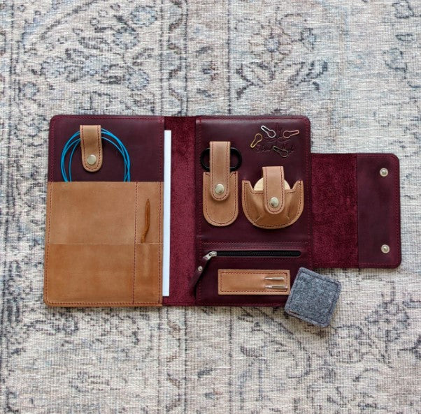 A wine red and whiskey leather notions case open faced to reveal the contents