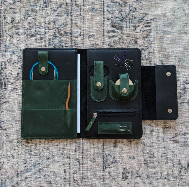 A hunter green and black leather notions case open faced to reveal the contents