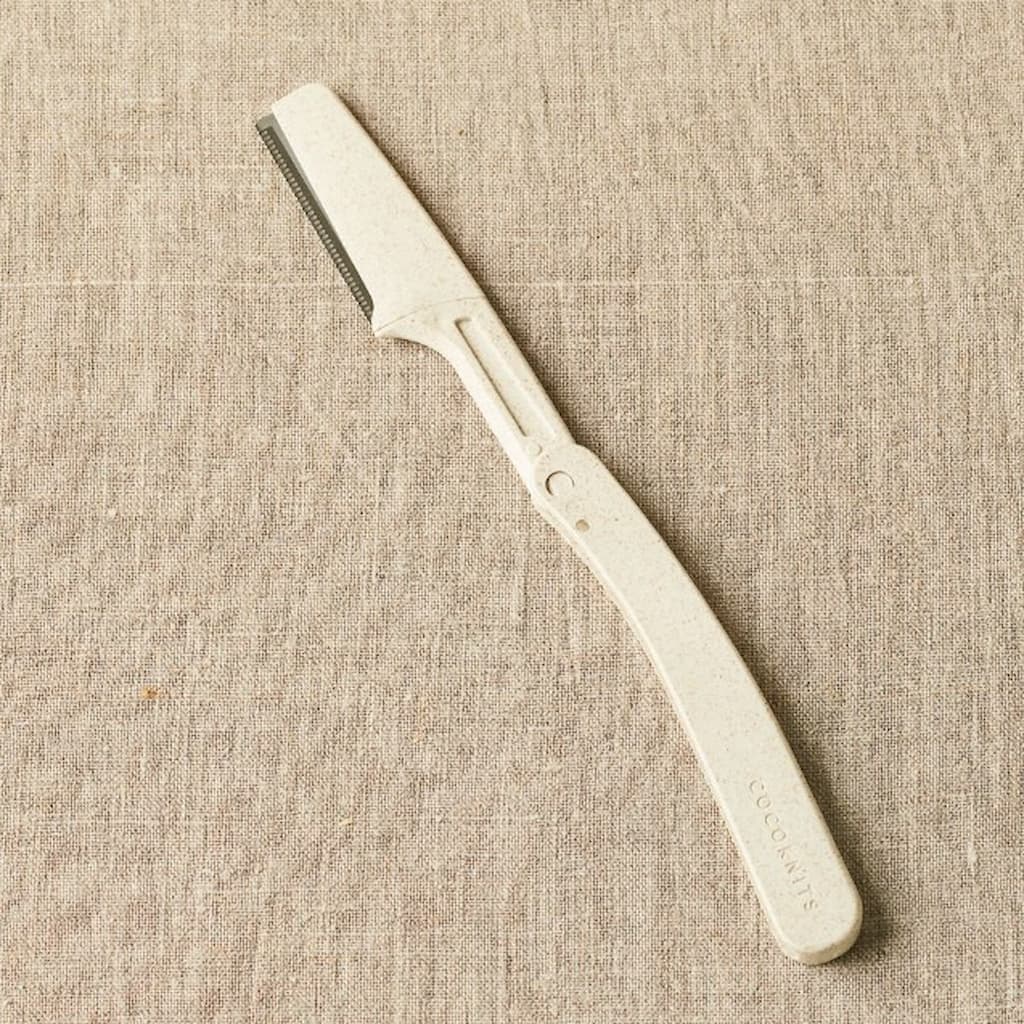 The Original Fuzz Off Comb laid against a beige fabric surface