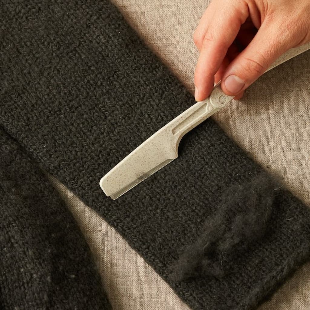 A cocoknits Fuzz Off Comb depicted cleaning a knitted garment of fuzz.