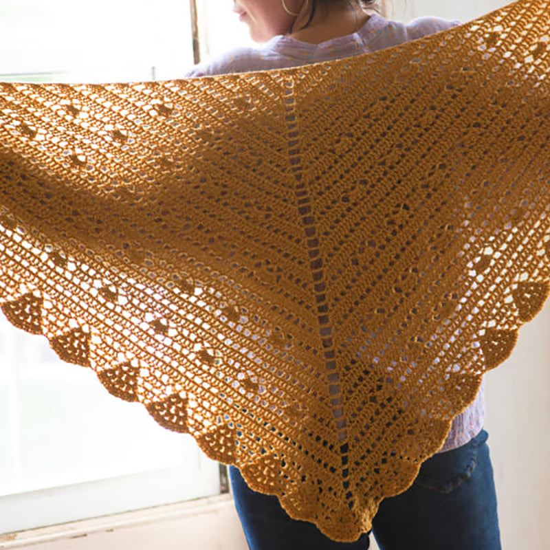 The crochet Cressida Shawl being held up by a woman facing away from the camera.
