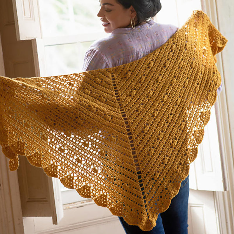 A woman holding the crochet Cressida Shawl and admiring it.