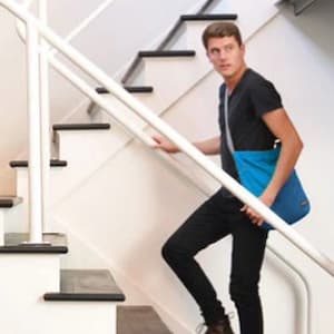 A man ascending stairs wearing a blue Flip & Tumble cross over bag.