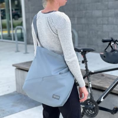 A person wearing a grey Flip & Tumble cross body bag from a back view.