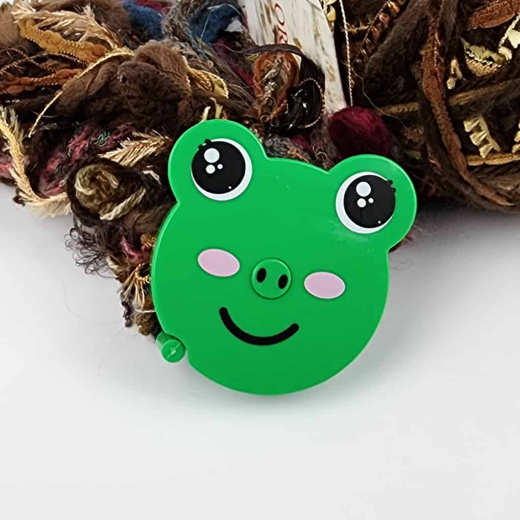 A small cutesy depiction of a frog on a circular tape measure.
