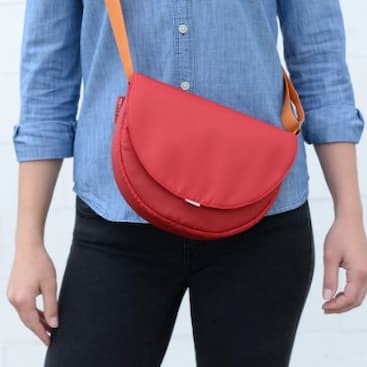 A person wearing a Flip & Tumble little purse cross body. Purse is red.