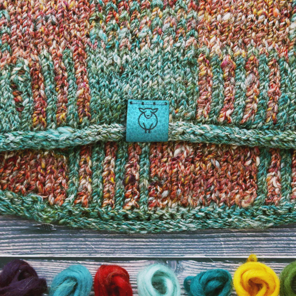 A knit cowl using Tweedy Merino Camel Fiber Blends, featuring the Turquoise logo suede tag.