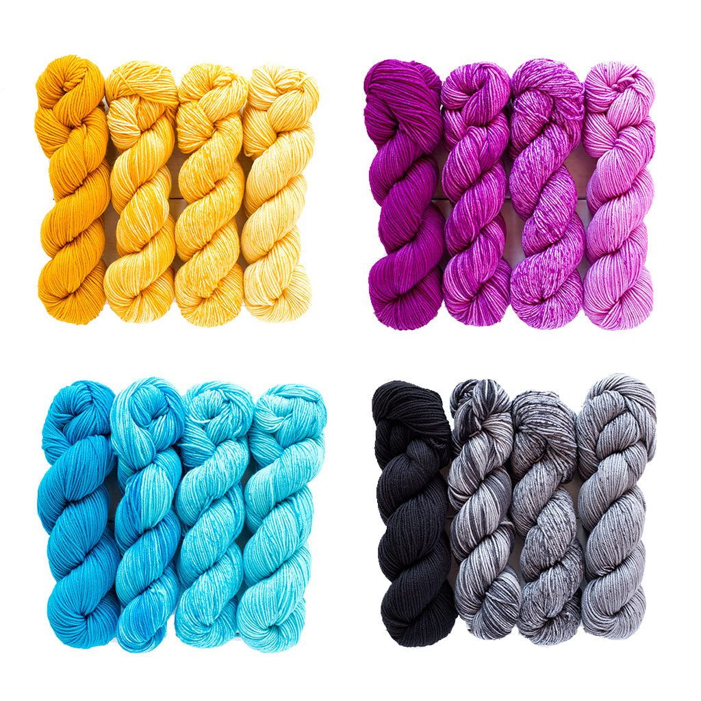 A group of yellow, purple, blue, and black uneek urth yarns merino gradient yarn kits.