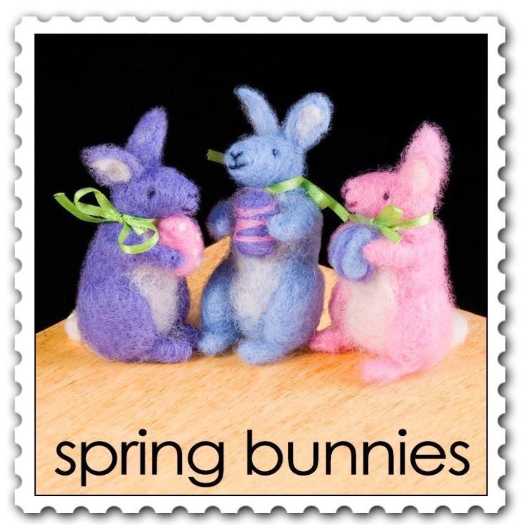 Woolpets spring bunnies needle felting kit- a pack of three pastel colored bunnies in the shades purple blue and pink all wearing a green ribbon around their necks and holding a little colored egg